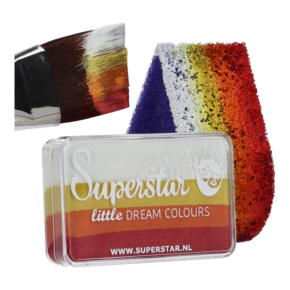 A paintbrush with red, yellow, and white strokes rests next to a glittery rainbow sponge. Nearby is a clear Face Paint & Body Paint Aqua Superstar - Little Magic Sunrise case by Infinity Faces, featuring vibrant, cruelty-free water-based makeup similar to the rainbow paints inside.