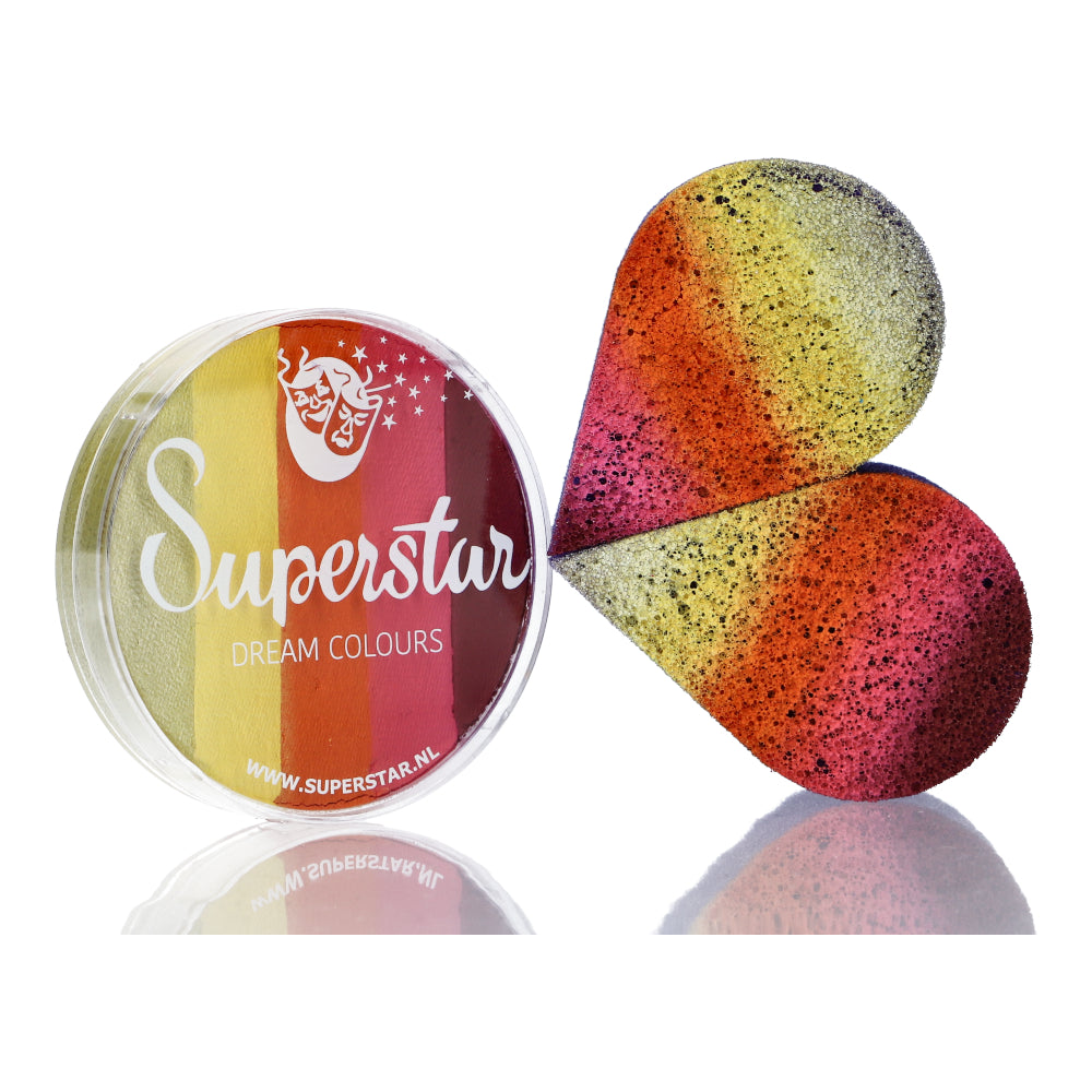 The Split Cake Dream Colour Superstar - Summer by Infinityfaces is a round 45gr container with a transparent lid, revealing red, orange, yellow, and black stripes. A heart-shaped sponge mirrors the vibrant pattern. It complies fully with the European Cosmetics Directive.
