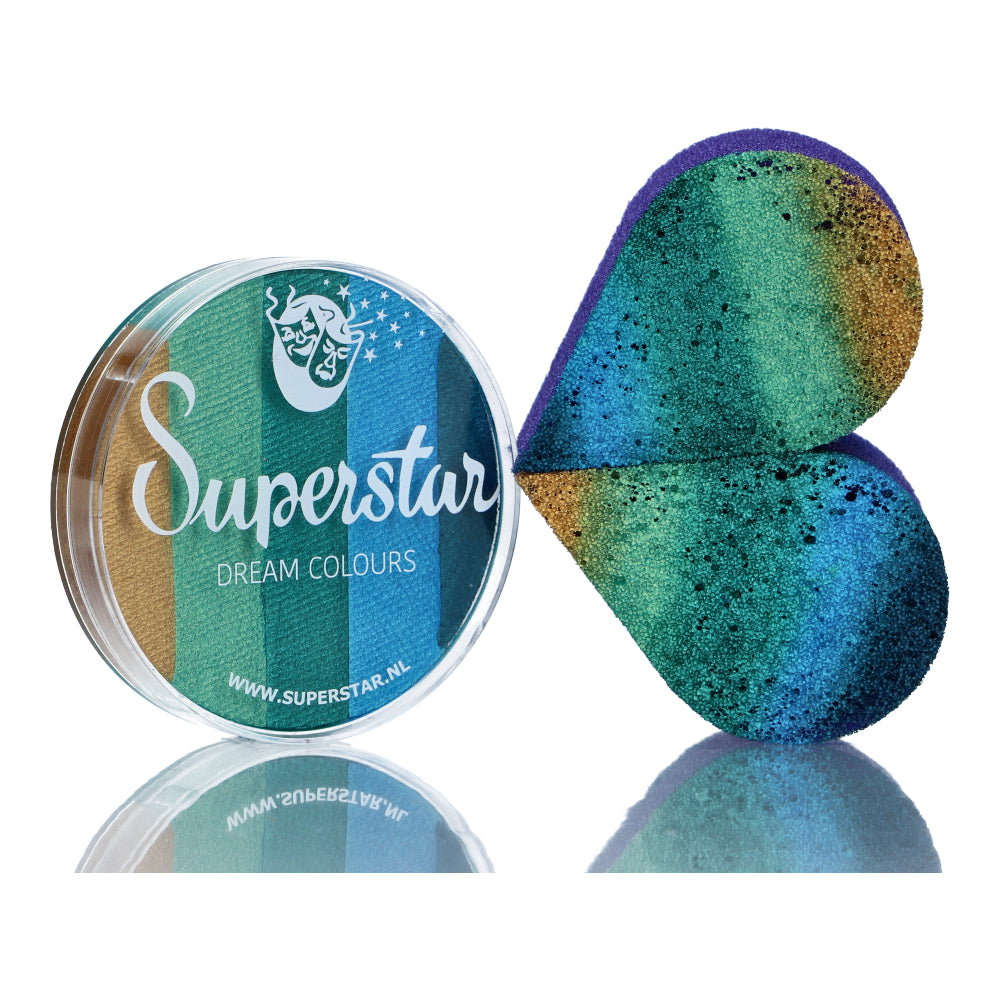A half-open round container of Split Cake Dream Colour Superstar - Emerald (45gr) by Infinityfaces reveals a green, blue, and gold gradient. Beside it sits a heart-shaped sponge with matching colors. Compliant with the European Cosmetics Directive for safe use.