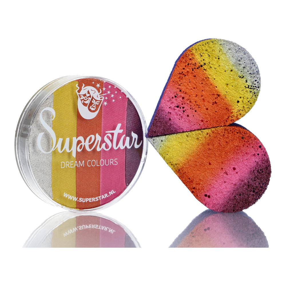 A round container of Infinityfaces Split Cake Dream Colour Superstar - Sunshine (45gr) sits next to a heart-shaped sponge. The vivid yellow, orange, pink, purple, and black stripes promise vibrant artistry. Its lid features the logo and website, ensuring compliance with the European Cosmetics Directive.