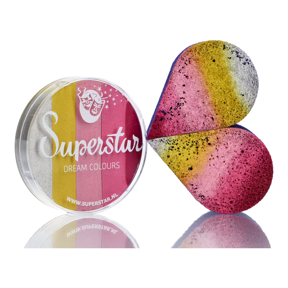 An open circular Infinityfaces Split Cake Dream Colour Superstar - Sweet (45gr) reveals a vibrant half-split heart sponge. The cake displays stripes of white, pink, yellow, and gold; the sponge is speckled with yellow, silver, pink, and black.
