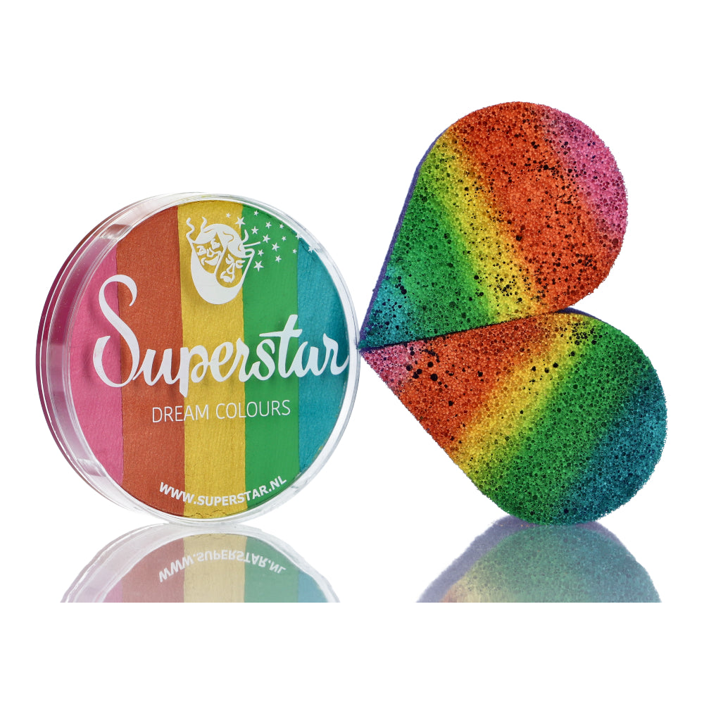 A circular container with a transparent lid, labeled Split Cake Dream Colour Superstar - Carnival (45gr) by Infinityfaces, sits beside a heart-shaped sponge. Both are designed for Aqua Face and Bodypaint, showcasing vibrant rainbow colors: red, orange, yellow, green, blue, and purple.