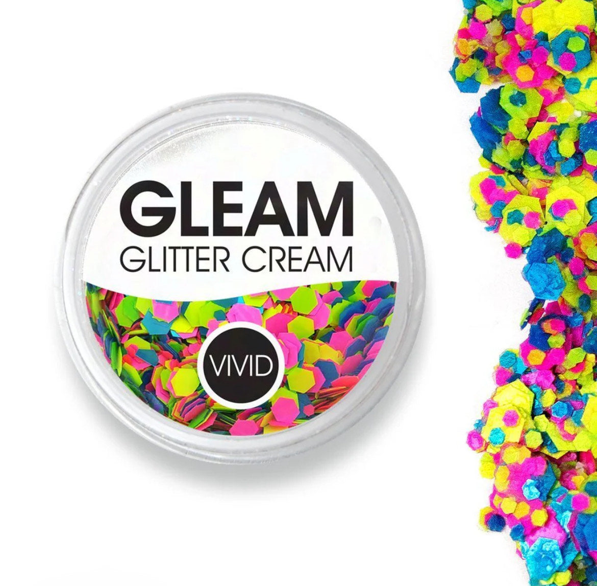 A round Infinity Faces Glitter Cream Gleam - Candy Cosmos UV (10g) container holds chunky neon pink, yellow, blue, and green glitter, with some glitter scattered on a nearby white surface.
