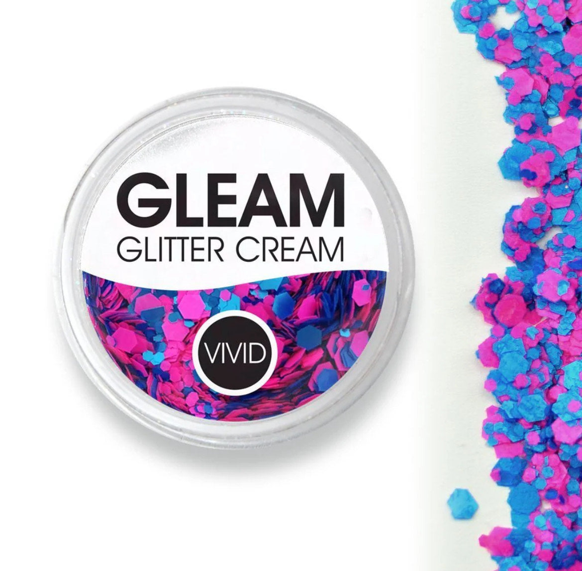 A round container labeled Infinity Faces Glitter Cream Gleam - Gum Nebula (10g), filled with chunky pink and blue glitter, sits beside a scattered pile of the same glitter on a white background.