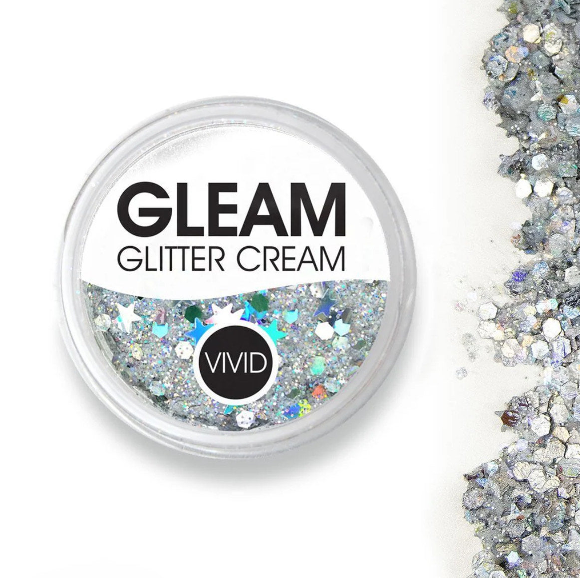 A round container of Infinity Faces Glitter Cream Gleam - Heaven (10g) filled with silver and holographic chunky glitter sits next to a scattered pile of glitter on a white background.