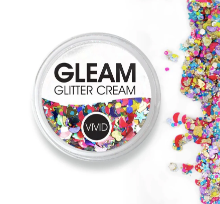 An open round container of Infinity Faces Glitter Cream Gleam - Festivity (10g) displays vibrant chunky glitter pieces spilling onto a white surface.
