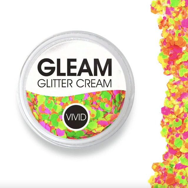 A round container labeled Infinity Faces Glitter Cream Gleam - Ignite (10g) with bright neon glitter inside; neon glitter is also scattered on the right side of the white background.