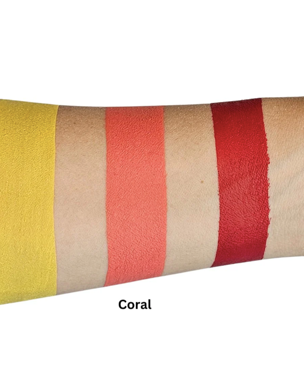 An arm shows three horizontal swatches—yellow, Prime Coral, and red—of Infinity Faces Face Paint & Body Paint Aqua Fusion (32g). Prime Coral is labeled under the middle swatch on a light background.