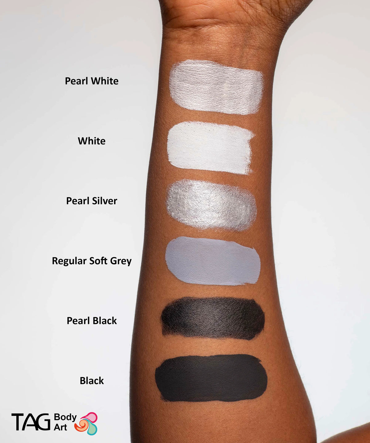 A forearm with six swatches of face paint, including TAG Face & Body Paint - Pearl White (32g), labeled from top to bottom as Pearl White, White, Pearl Silver, Regular Soft Grey, Pearl Black, and Black.