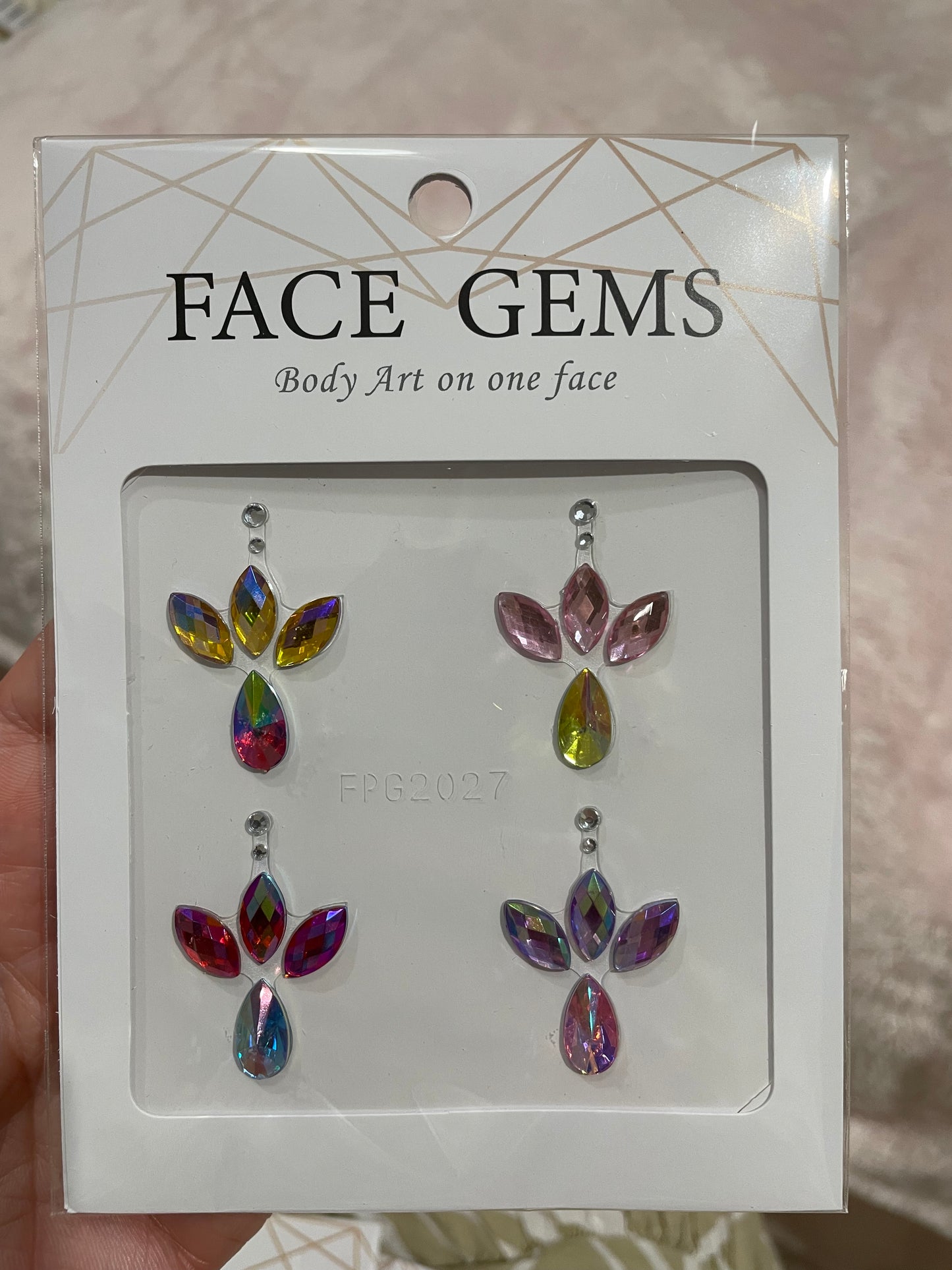 A package of Infinityfaces Face- & Body Gems - Teardrops features four colorful adhesive flower-shaped gem sets in pink, blue, yellow, and purple. The adhesive allows for multiple uses and easy removal for skin cleansing.