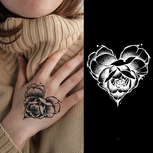 A person in a beige turtleneck displays the Temporary Herbal Tattoo - Fall in Love by Infinityfaces, featuring a black floral design on their hand. Beside it lies a white heart-shaped version on a black background.