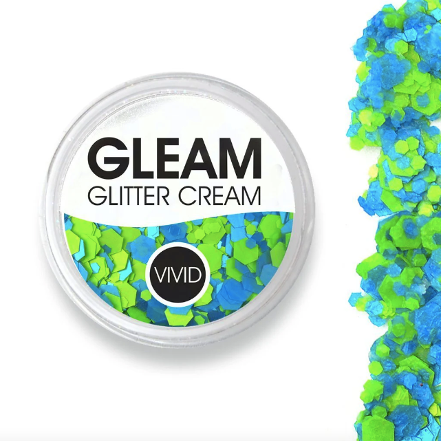 A round container labeled Infinity Faces Glitter Cream Gleam - Nu-Ocean UV (10g) holds chunky blue and green glitter cream. Loose glitter is scattered to the right of the container on a white background.