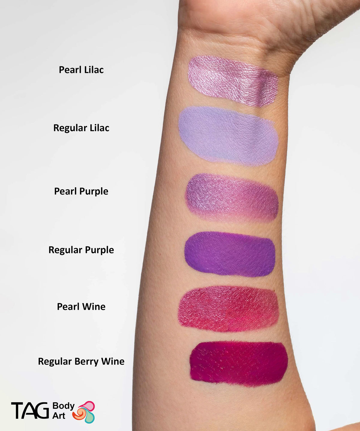 Six swatches of purple-toned face paint on a forearm, featuring TAG Face & Body Paint - Pearl Purple (32g) alongside lilac, purple, wine, and berry wine shades.