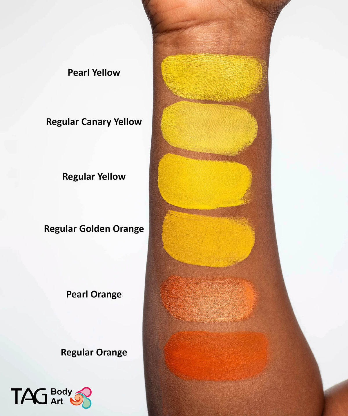 Six TAG Face & Body Paint - Pearl Orange (32g) swatches ranging from yellow to orange applied to a person’s inner forearm, with color names labeled beside each.