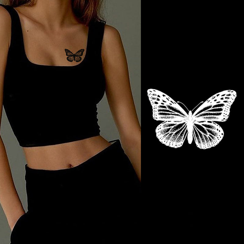 A person in a black crop top displays a striking Temporary Herbal Tattoo - Butterfly by Infinityfaces on their chest, mirrored by an illustration of a white butterfly against a black background.