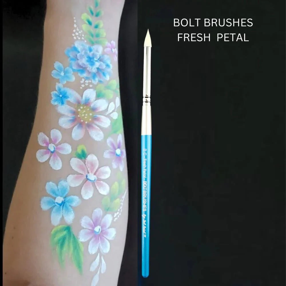 A painted arm with vibrant flowers and leaves is shown beside an Infinity Faces Brushes Bolt - Diamond Collection - Fresh Petal paintbrush, featuring a blue handle and white bristles, all set against a black background.