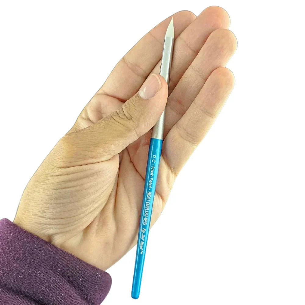 A hand wearing a purple long-sleeve shirt holds the Infinity Faces Brushes Bolt - Diamond Collection - Fresh Petal against a white background.